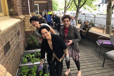 Three women stand next to a planter box.