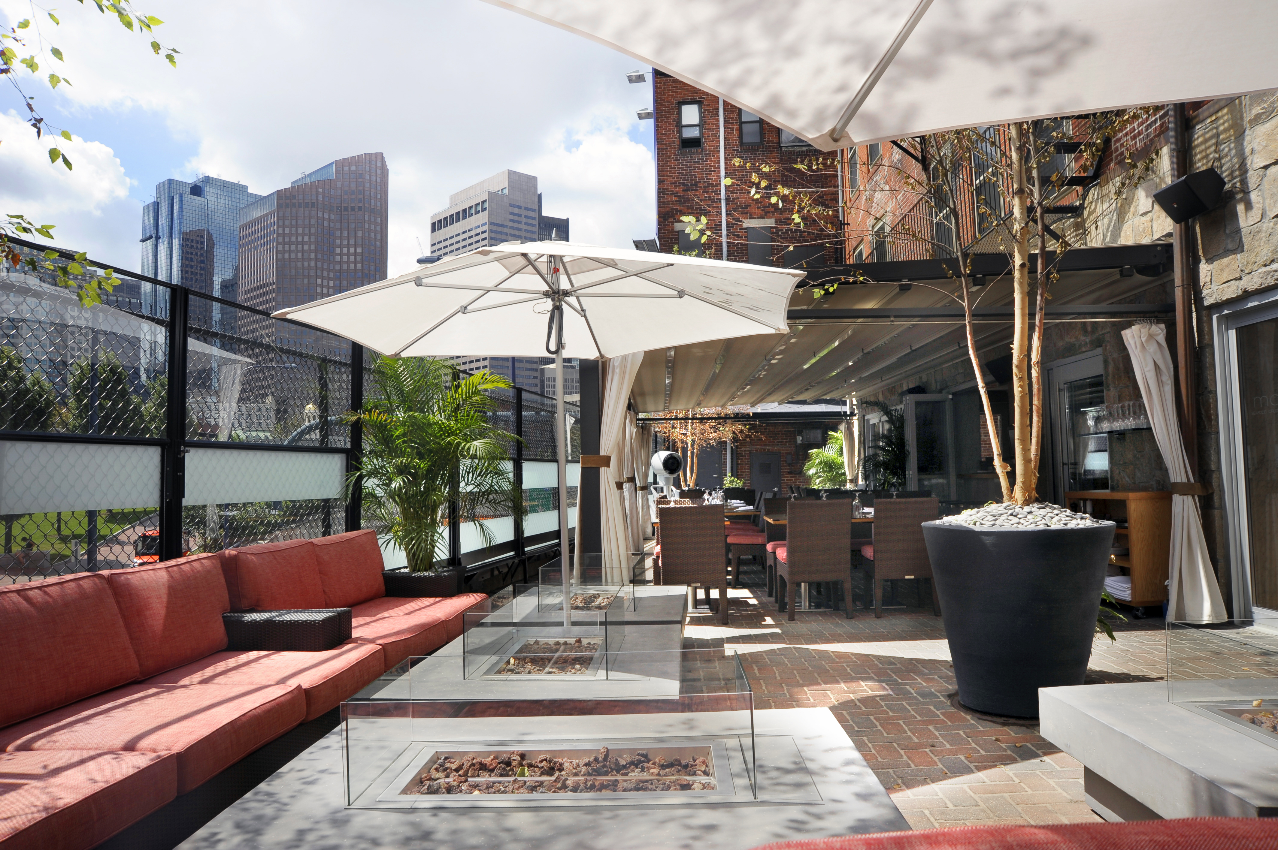 A restaurant’s outdoor patio with fire pits, white umbrellas, and lounge seating with red cushions