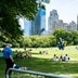 Several people enjoying the sun in Central Park with a fence and red sign reading "Keep This Far Apart" in the foreground