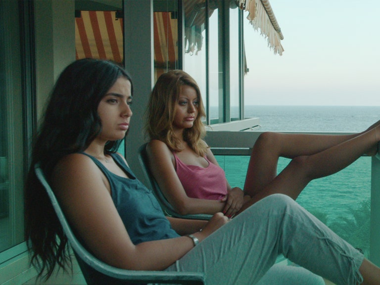 Film still: two people sit on balcony.