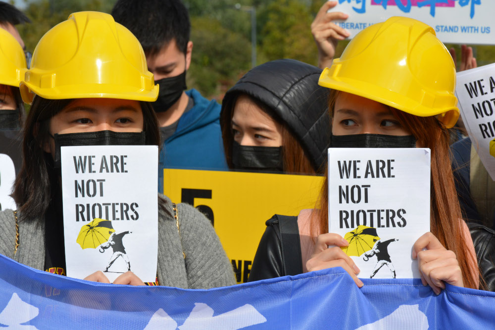 Protesters in yellow helmets hold 'we are not rioters' leaflets, in solidarity with Hong Kong