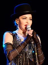 Madonna in a bejeweled dress, black gloves on her hand and a top hat, singing onstage.