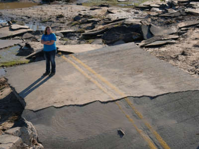 A woman stands on asphalt rubble of what was once a road