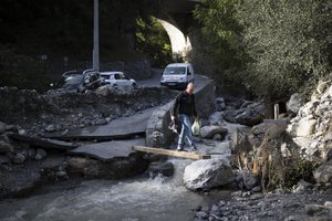 A resident walks over a stream wih supplies in Breil-sur-Roya, near the border with Italy, Monday, Oct. 5, 2020. Flooding has devastated mountainous areas in France's southeastern region of Alpes-Maritimes and Italy's northwestern regions of Liguria and Piedmont, after a storm swept through the two countries on Friday and Saturday.