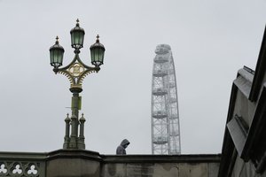 A man wearing a face mask to try to curb the spread of coronavirus walks over Westminster Bridge backdropped by the London Eye ferris wheel, on a rainy day in central London