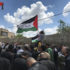 Protesters gather, a Palestinian flag flying, little girl on her fathers shoulders.