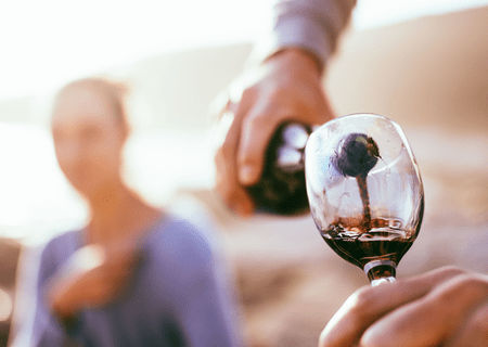 Hands pouring wine with blurry woman in background.