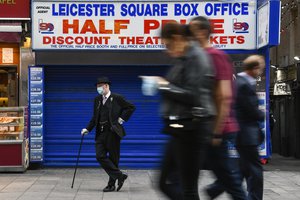 File - A man wears a face mask in Leicester Square, as people walk past, in London, Tuesday, Sept. 22, 2020. Prime Minister Boris Johnson has announced that pubs and restaurants closing at 10pm, due to the spike of cases of coronavirus across the United Kingdom.