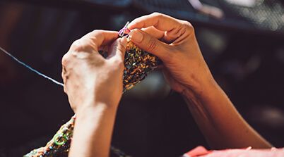 A pair of hands, knitting a multicolor scarf