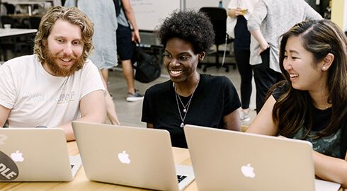 A diverse group of people discussing code on their laptops