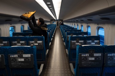 A traveler places his bag in an overhead luggage rack in a bullet train bound for Kyoto and Osaka at Tokyo Station in Tokyo.