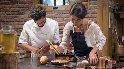 A man and a woman, both chefs, carefully arranging elements of a butternut squash quiche