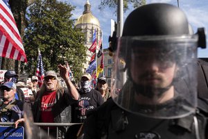 An officer in riot gear stands between supporters of President Donald Trump and counter protesters as the groups yell at each other outside of the Georgia State Capitol in Atlanta on Saturday, Nov. 21, 2020.