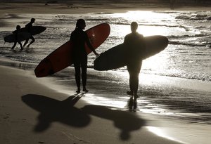 In this April 28, 2020, photo, surfers walk the beach in Sydney, Australia. Police in Australia say a 60-year-old surfer has been attacked and killed by a 10-foot shark off the coast of northern New South Wales state.