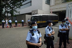 File - A protester, second left at the back, gestures with five fingers, signifying the "Five demands and not one less" in front of the prison van carrying former Studentlocalism leader Tony Chung outside a court, in Hong Kong, Thursday, Oct. 29, 2020.