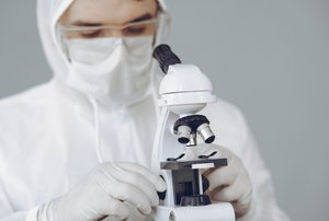 Photo of person wearing face mask and protective gear with a Coronavirus Covid-19 test sample for vaccine study