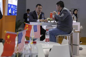 FILE - In this Nov. 6, 2019, file photo, visitors chat near American and Chinese flags displayed at a booth for an American company promoting environmental sensors during the China International Import Expo in Shanghai.