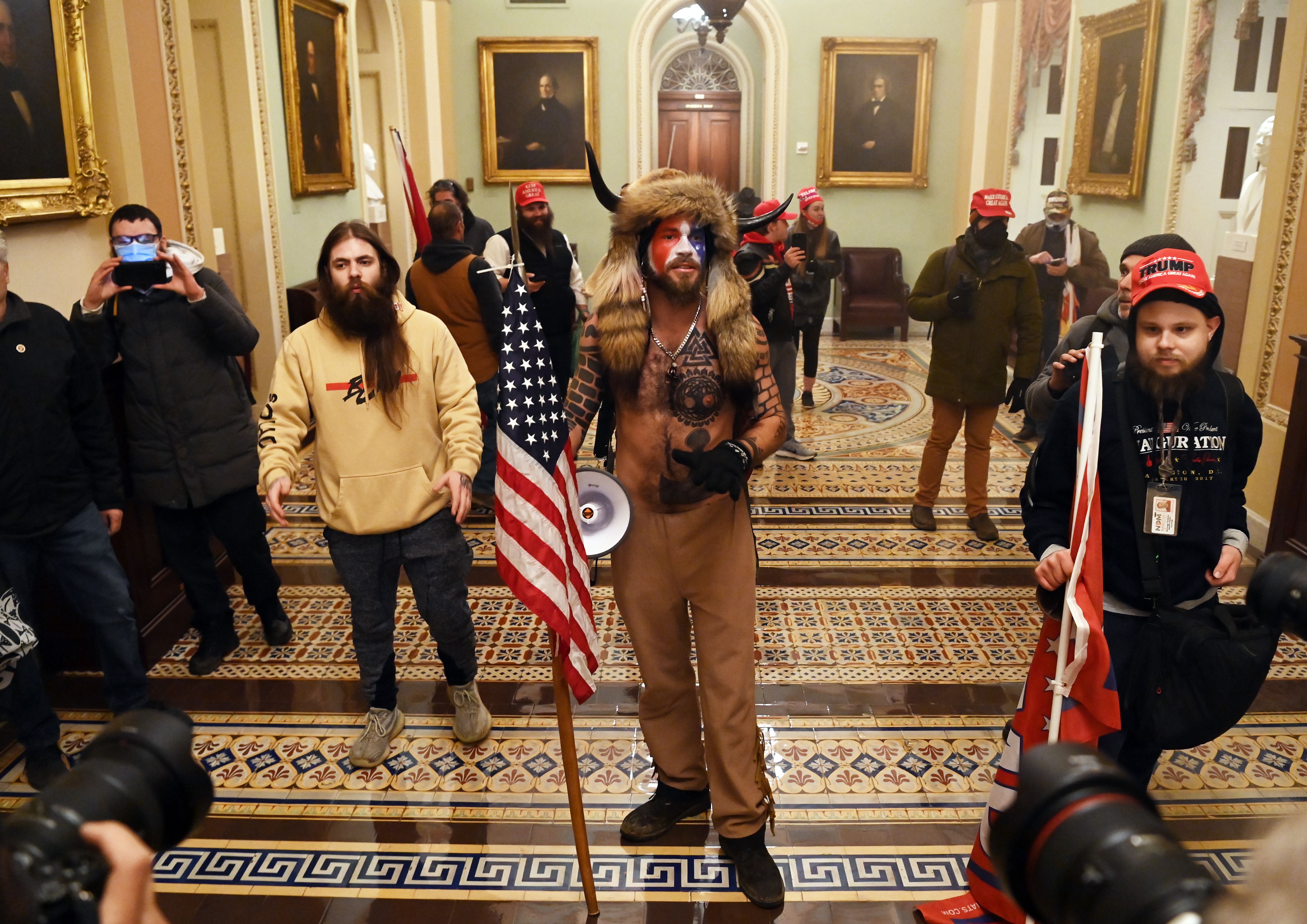 Members of the mob that broke into the US Capitol stand holding flags in a Capitol hallway.