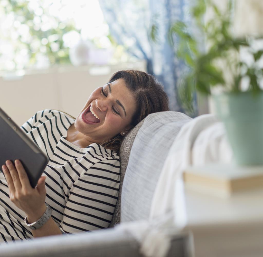 Frau liegt mit Tablet auf dem Sofa