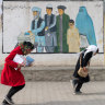 Girls head home from school in Kabul past a mural promoting voting for men and women.
