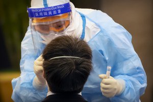 A worker in a protective suit gives a COVID-19 test to a foreign journalist covering a press conference for China's National People's Conference (NPC) at a hotel in Beijing, Thursday, May 21, 2020.