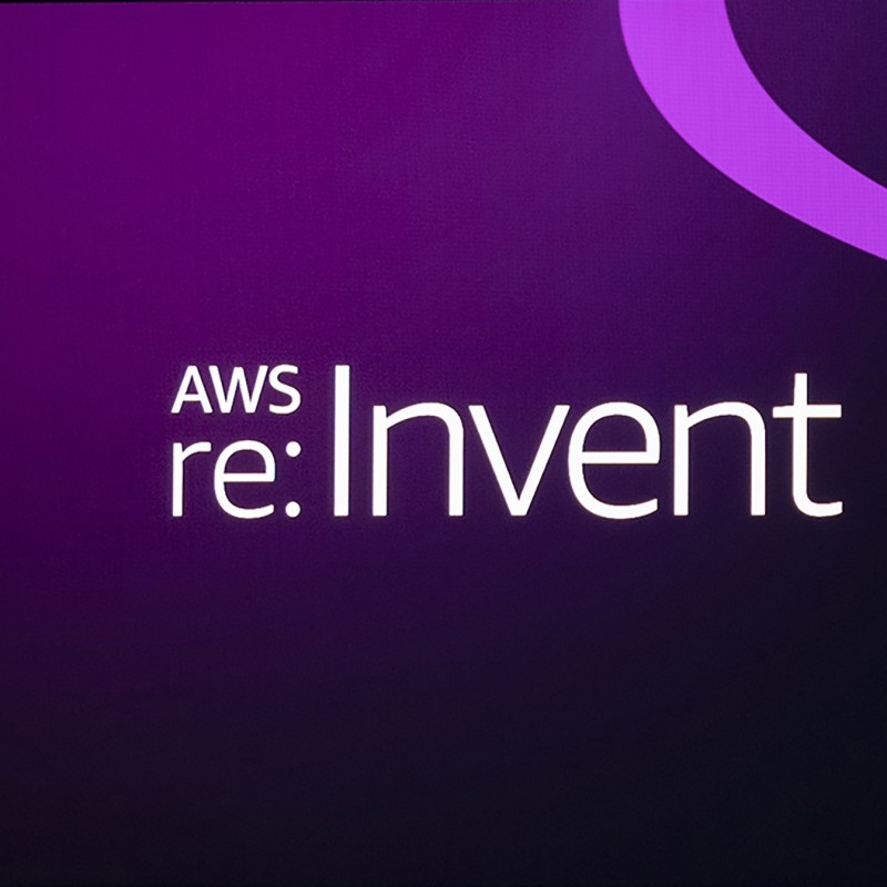 AWS re:invent logo on a purple gradiant background. To the right of the logo, streams of aqua and purple move appear to move fluidly across the image.