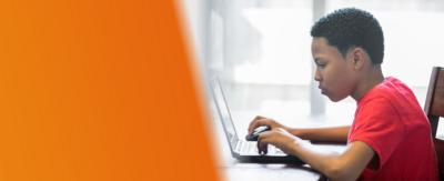 A boy is sitting at a desk looking at a computer.