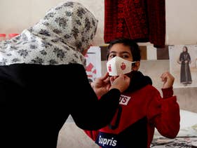 Suhad Saidam adjusts one of her face masks on a youth at her sewing workshop in Gaza City, December 14, 2020.
