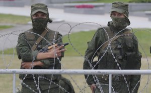 A serviceman gestures for unknown reason, standing behind a barbed wire fence during a protest in Minsk, Belarus, Sunday, Aug. 23, 2020.