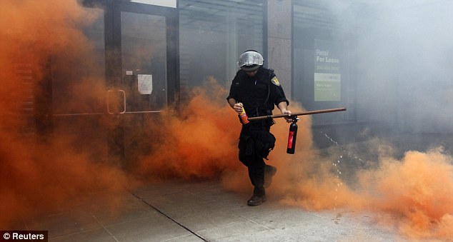 Burning: A police officer in riot gear emerges after shooting pepper spray at masked protestors when demonstrations turned violent in Seattle