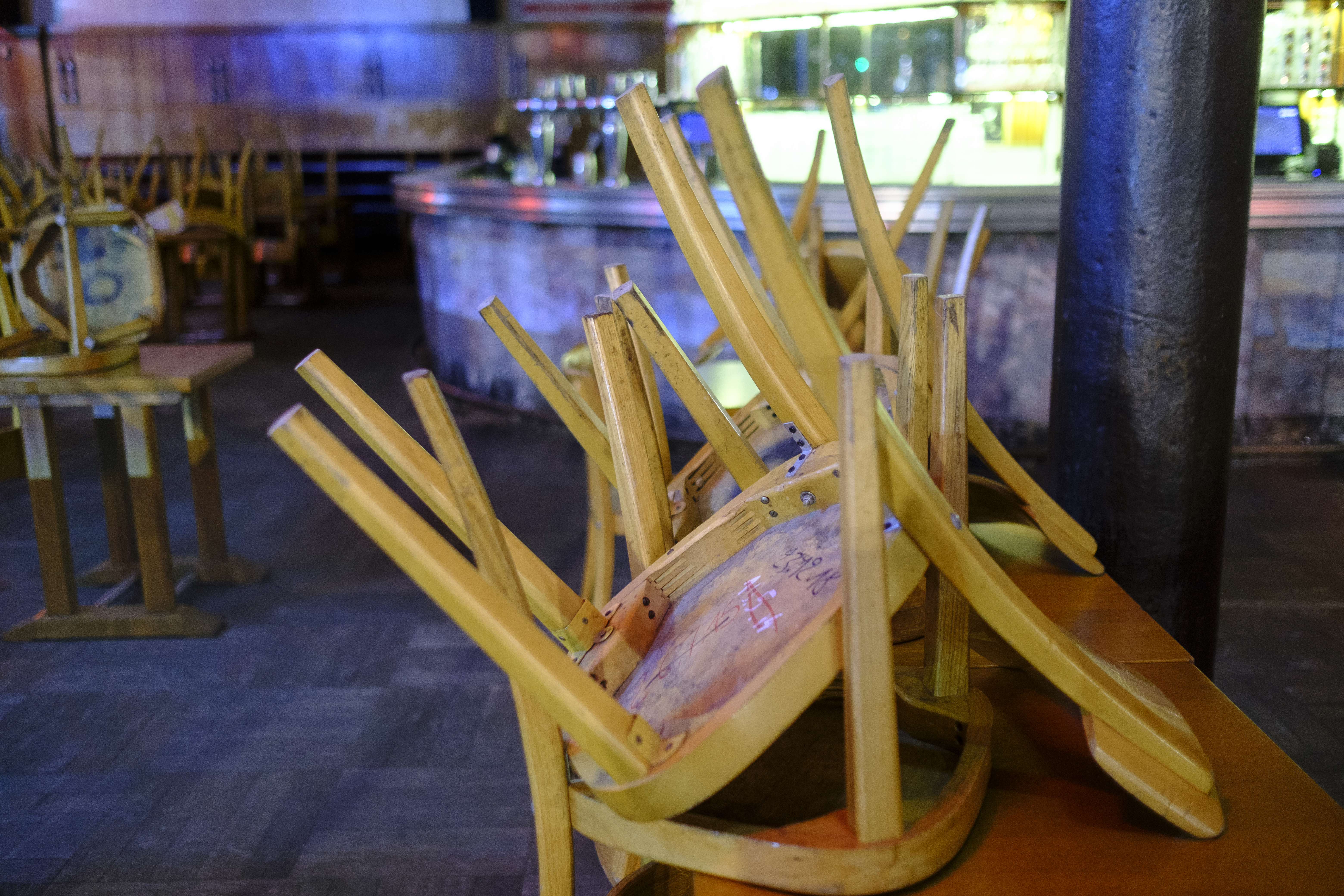 Wooden chairs appear stacked on a bar alongside a window in a closed restaurant.