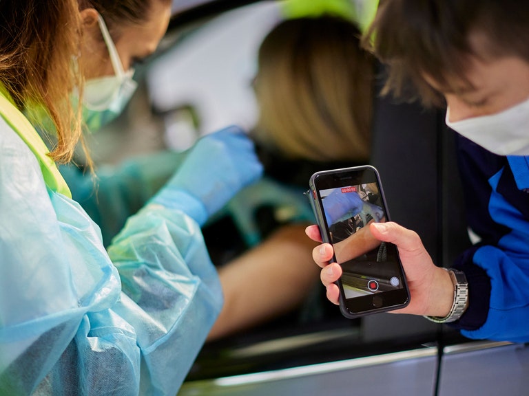 A boy records video on a phone of a woman receiving a vaccine shot