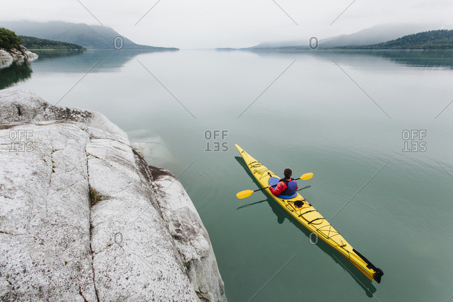 Female sea kayaker paddling pristine waters of Muir Inlet, overcast sky in distance, Glacier Bay National Park, Alaska