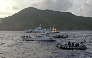 Japanese Coast Guard vessel and rubber boats, rear and right, sail alongside activists' boat, center with a flag, warning the activists away from a group of disputed islands called Diaoyu by China and Senkaku by Japan, early Sunday, Aug. 18, 2013.  Nearly two dozen Japanese nationalist activists and fishermen have sailed to a small group of islands at the center of a territorial dispute with China. They were closely monitored by Japan’s Coast Guard, but there were no Chinese patrols in the area and no incidents were reported. (AP Photo/Emily Wang)