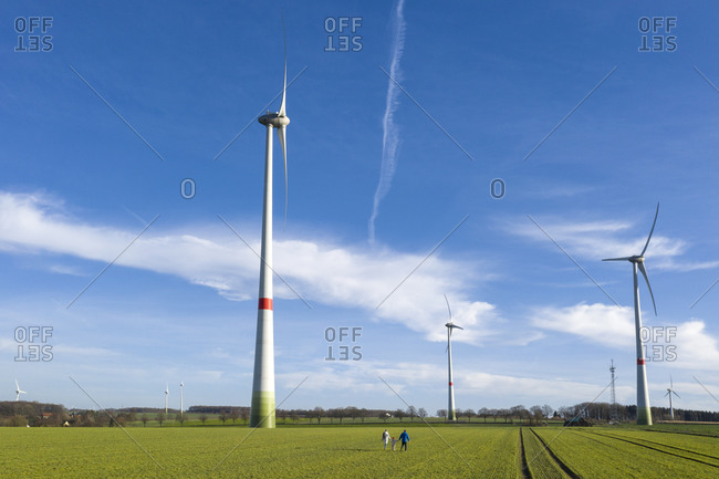 Back view of parents with little daughter walking on a field with wind wheels in the background