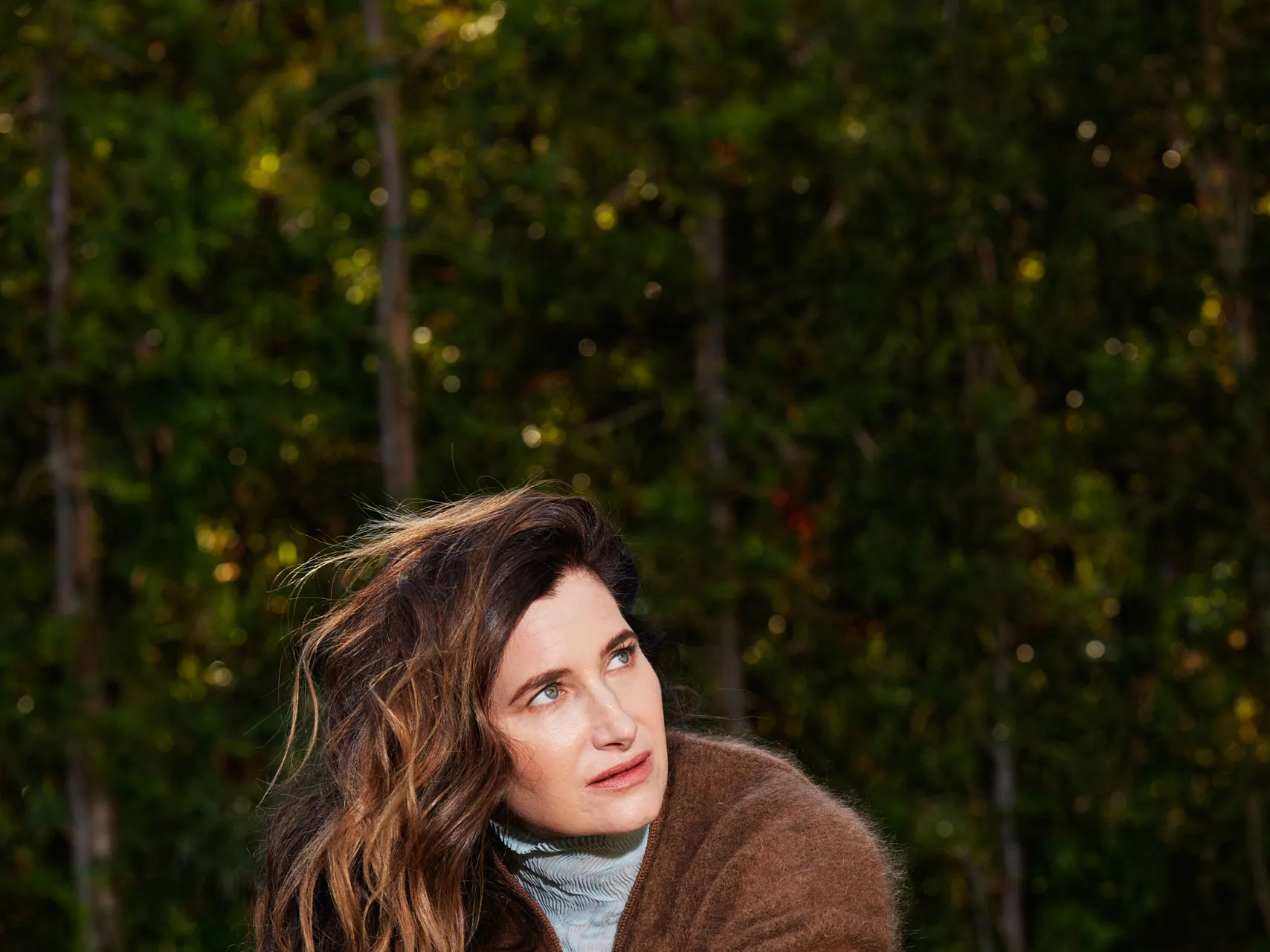 Kathryn Hahn sits crosslegged in the grass.