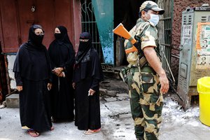 A paramilitary soldier stands guards as voters wait to cast their votes at a polling station during the fourth phase of West Bengal state elections in Kolkata, India, Saturday, April 10, 2021.