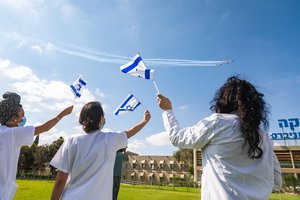 People wave Israeli flags during a Israel 72nd Independence Day - Israeli Air Force Fly By.