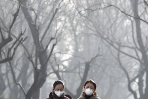 In this Dec. 19, 2016, file photo, women wearing masks to protect themselves from air pollution walk through Ritan Park shrouded by dense smog in Beijing.