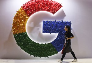 In this Monday, Nov. 5, 2018 file photo, a woman walks past the logo for Google at the China International Import Expo in Shanghai. By U.S. standards, the Justice Department's move to sue Google this week for abusing its dominance in online search and advertising was a bold move.