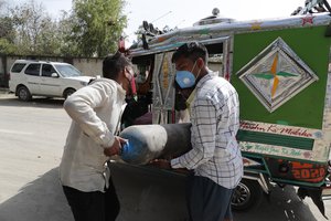 People carry a medical oxygen cylinder at a charging station on the outskirts of Prayagraj, India, Friday, April 23, 2021.