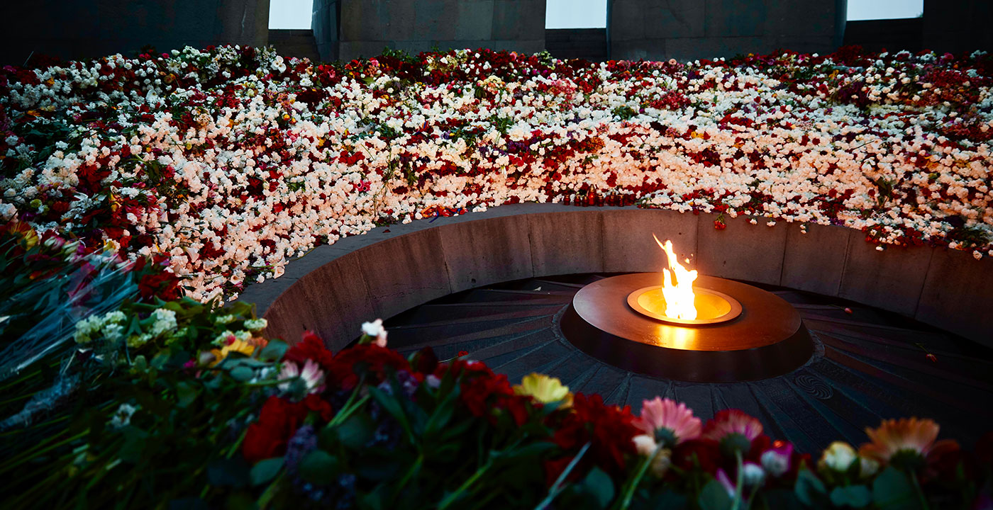 In a circular memorial monument, hundreds of cut roses in all colors form a circle around a lit flame.