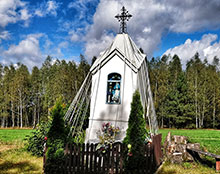 Outdoor shrine, like a miniature church, surrounded by ribbons, picket fence, and shrubs.