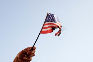 Capitol riot: Hand holding burning the American flag - a symbol of mass protests in the USA