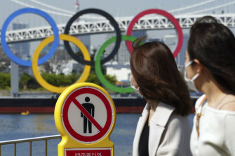 Women walk by a “no trespassing” sign at a park with a backdrop of the Olympic rings in Tokyo.