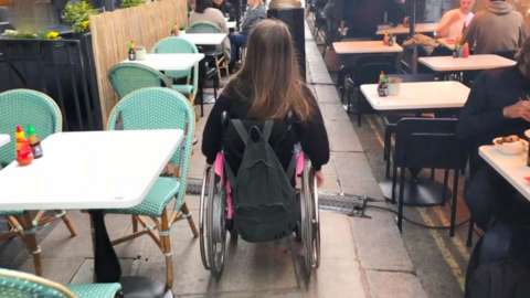 A wheelchair user navigates a crowded pavement