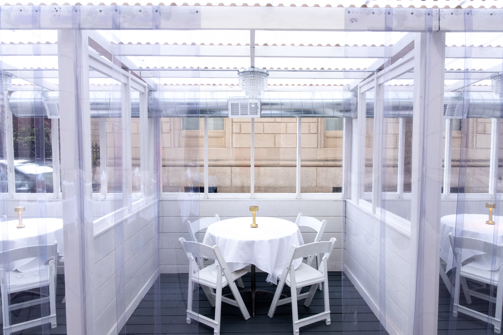 An enclosed outdoor seating area with a bright white interior, a round white table and table cloth with bright white patio chairs.