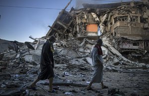 Palestinians walk next to the remains of a destroyed 15 stairs building after being hit by Israeli airstrikes on Gaza City, Thursday, May 13, 2021.