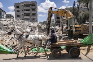 A horse-drawn cart is pulled past an worker using an hydraulic excavator to assist in reclaiming valuable materials from a debris pile of a building destroyed by an airstrike prior to a cease-fire reached after an 11-day war between Gaza's Hamas rulers and Israel, in Gaza City, Saturday, May 22, 2021.