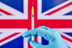 Hand in medical gloves holds syringe with Covid-19 vaccine over the Great Britain flag